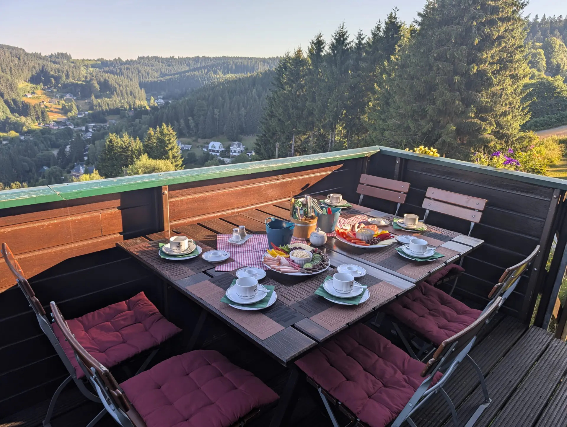 Gedeckter Frühstückstisch auf einem Balkon mit Panoramablick über ein grünes Waldtal.