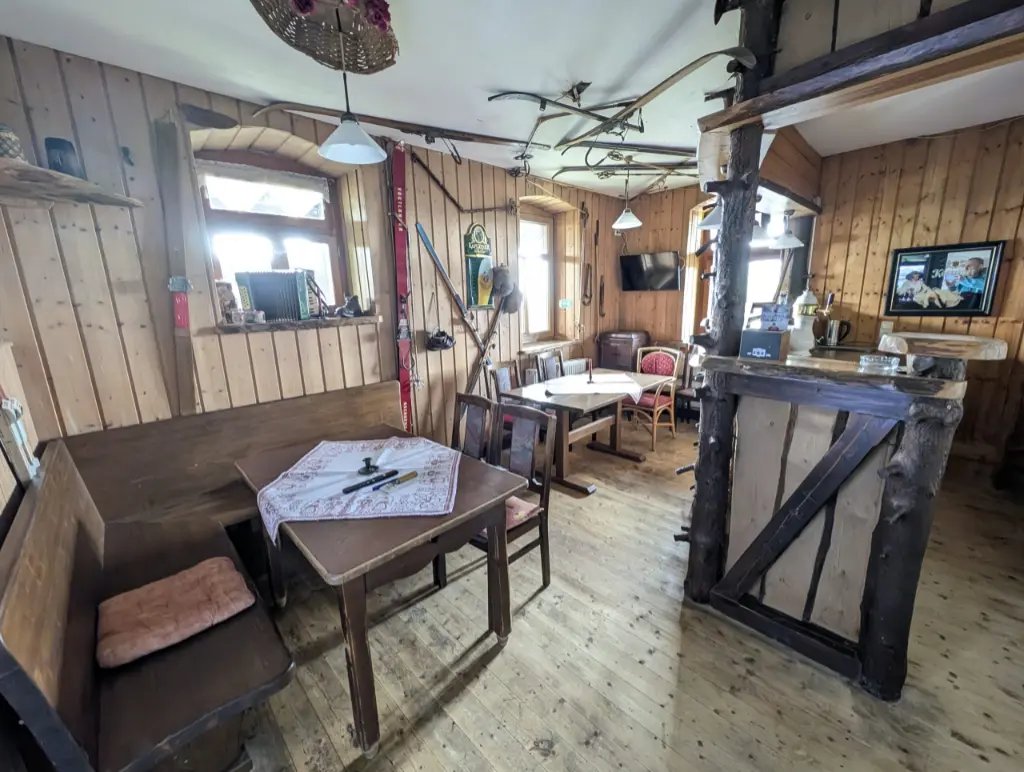 Skibar Klingenthal Rustikal gestaltete Skibar mit Holzvertäfelung, Holztischen und einer Theke aus naturbelassenen Baumstämmen. An den Wänden und an der Decke hängen historische Holzski und Skistöcke als Dekoration.