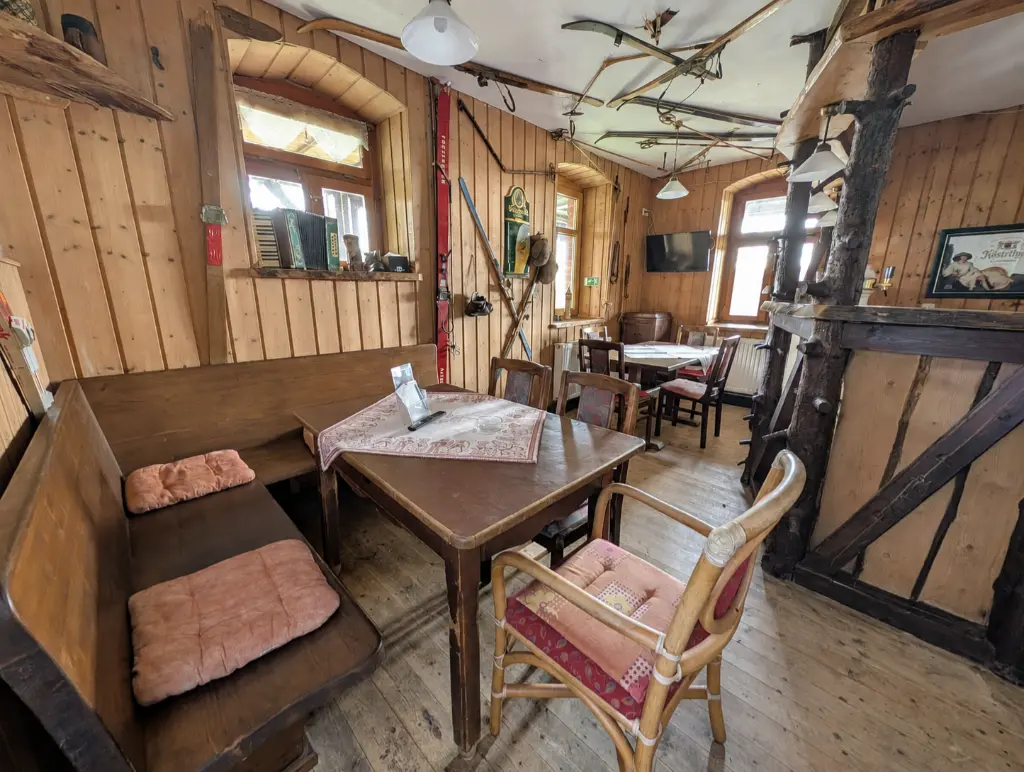 Rustikal gestaltete Skibar mit Holzvertäfelung, Holztischen und einer Theke aus naturbelassenen Baumstämmen. An den Wänden und an der Decke hängen historische Holzski und Skistöcke als Dekoration.