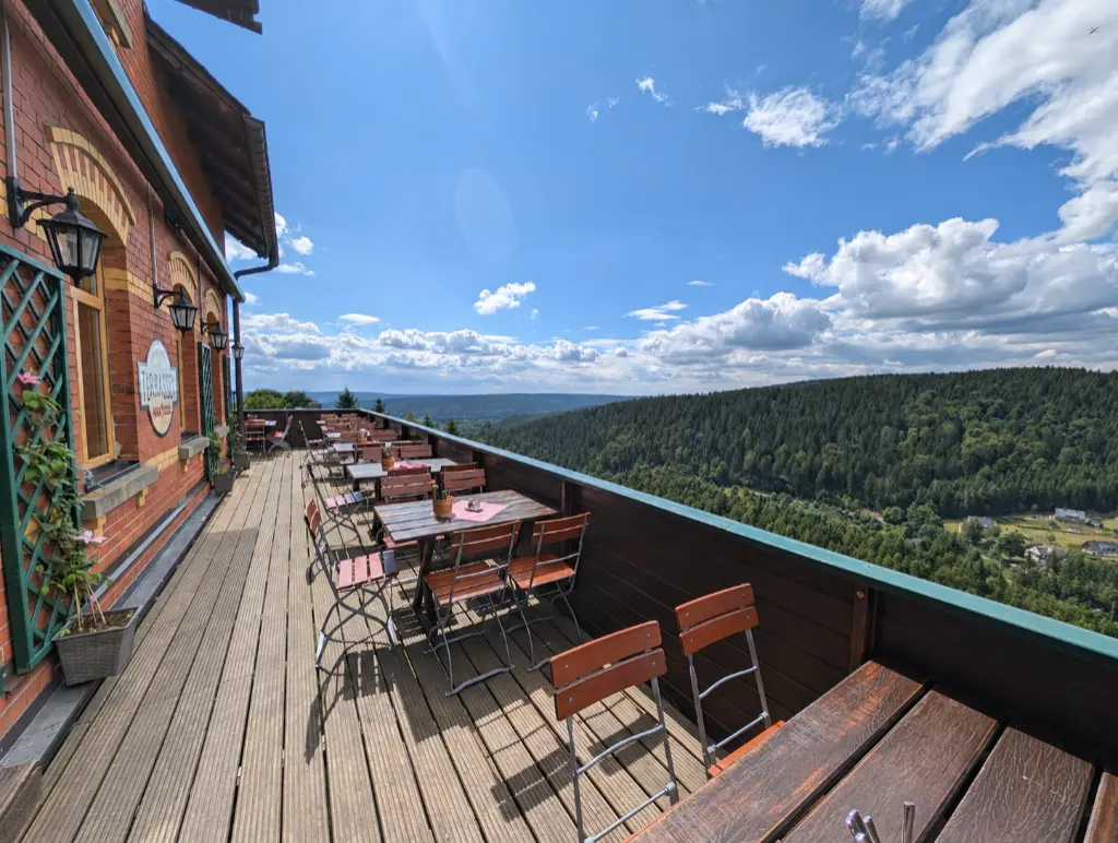 Terrasse Gedeckter Frühstückstisch auf einem Balkon mit Panoramablick über ein grünes Waldtal.